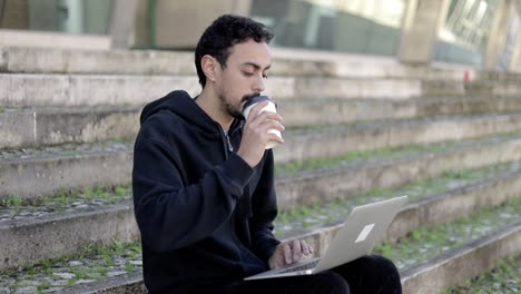 Man-holding-paper-cup-and-using-laptop